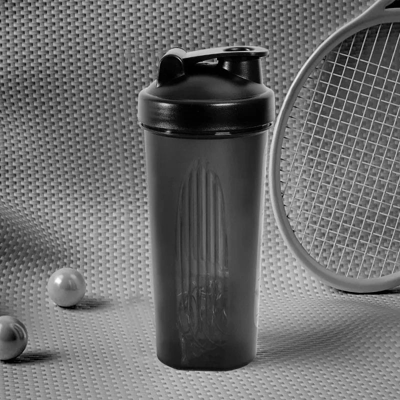 Black protein shaker bottle on a textured surface with a racket and balls in the background