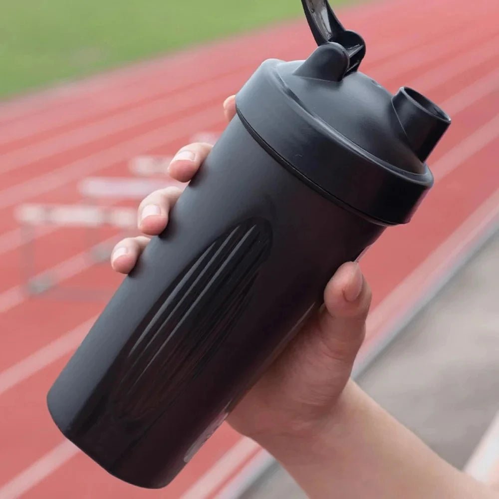 Person holding a black water bottle with a shaker top on a track background